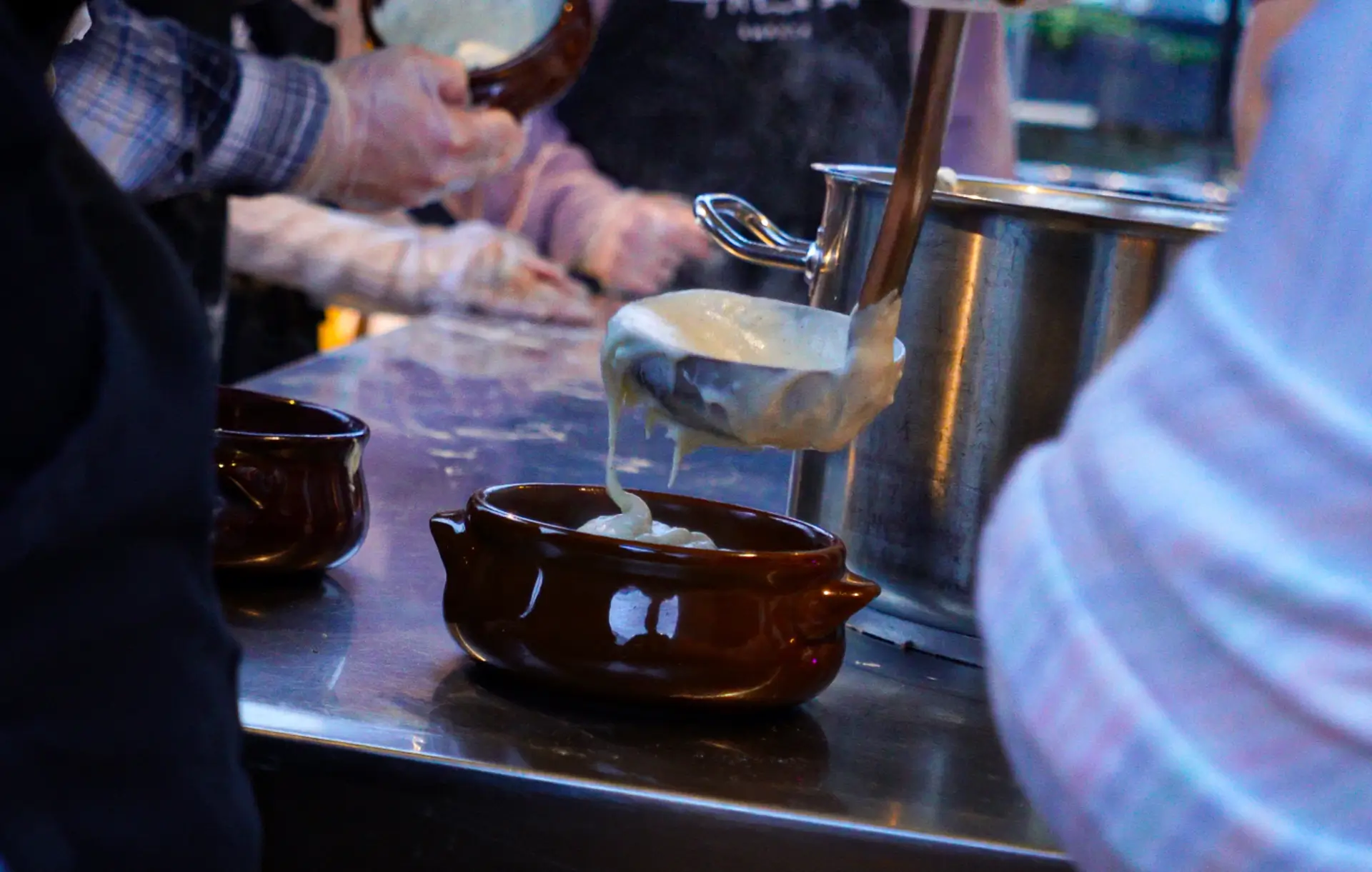 Hot béchamel sauce being poured over moussaka — the final touch